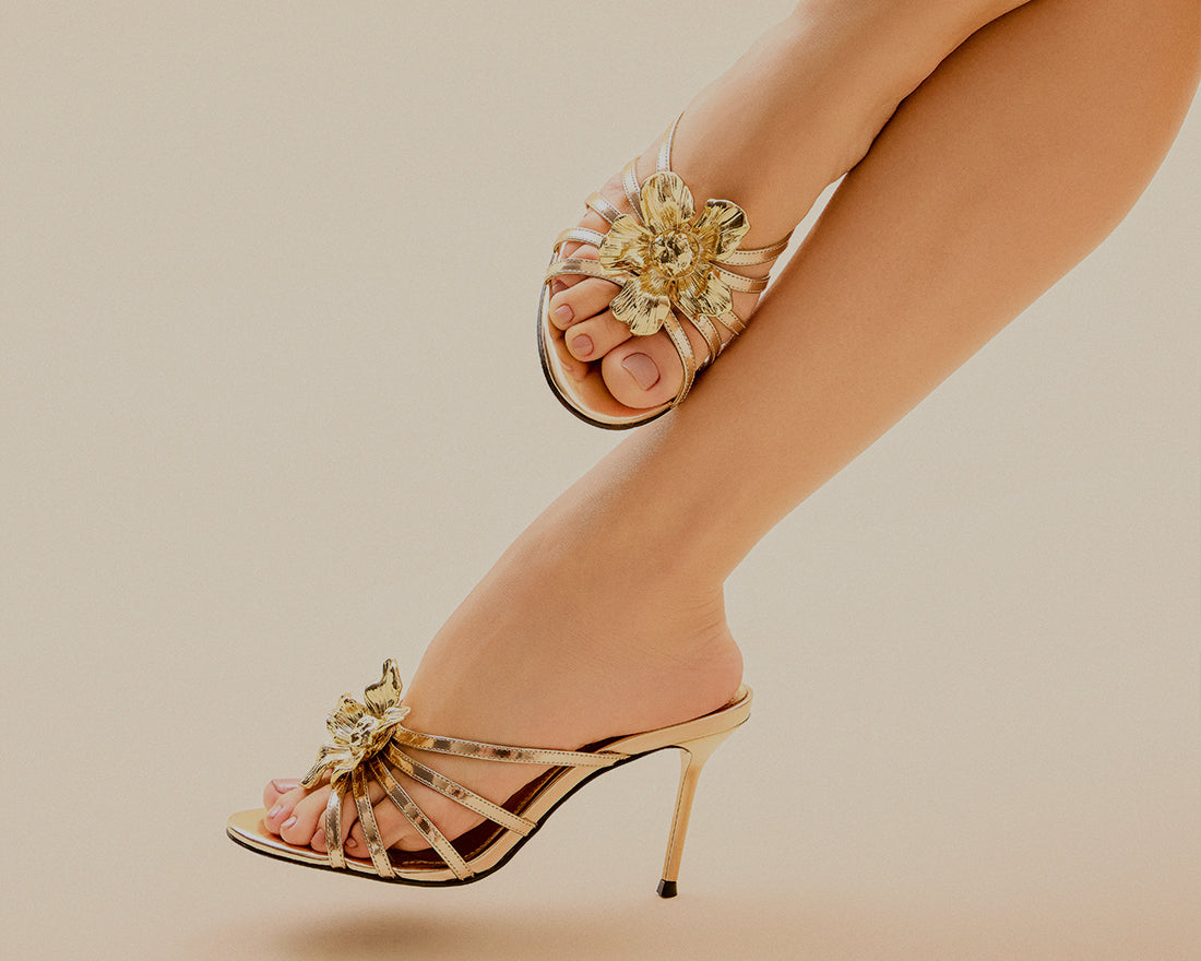 Model wearing gold metallic high-heeled sandals with floral detail, with the text “Gold Rush” and “Shop Metallics.”