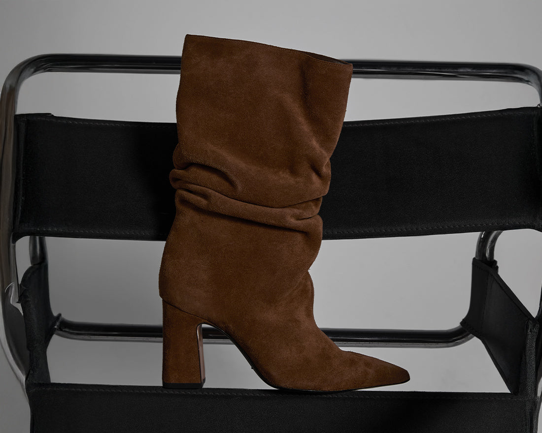 Brown suede slouchy boots elegantly placed on a modern black chair, highlighting the return of one of Schutz’s most iconic and versatile winter styles.