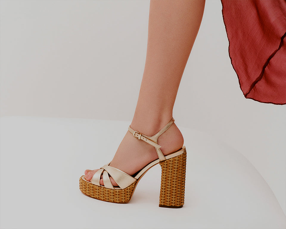 Model showcasing metallic gold platform high-heeled sandals with a woven block heel and delicate ankle strap, styled with a flowing red dress, highlighting new summer fashion arrivals.