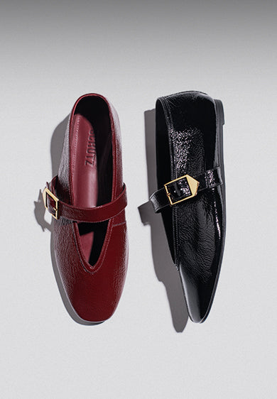 Two flat ballerina shoes side by side on a light background, one in deep red and the other in glossy black, both featuring gold buckles, with the word 'BALLERINAS' on the left.