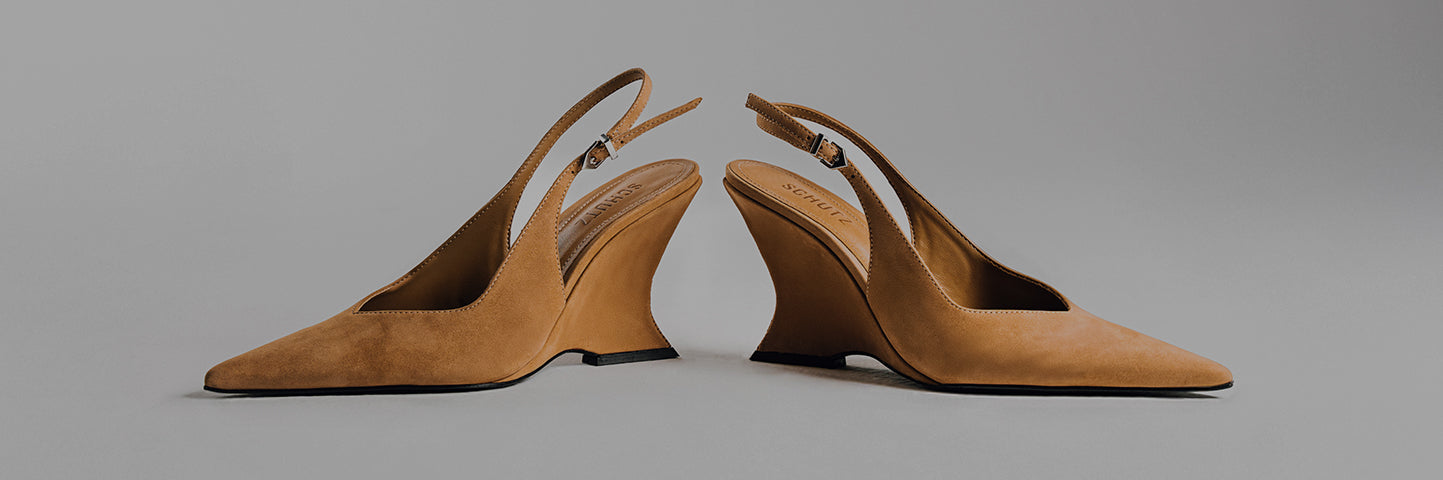 A close-up shot of two tan suede slingback wedge heels with a distinctive, sculptural, curved wedge heel. The text "SCULPTURAL HEEL" is prominent on the left side of the image.