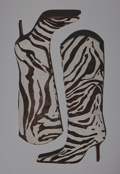 A close-up shot of the lower portion of a pair of high-heeled boots and possibly a matching bag, all made of white and dark brown zebra-print hair-on hide material. The boots have a square toe and a tall, brown stiletto heel. The text "WILD STYLES" is overlaid in the center of the image.