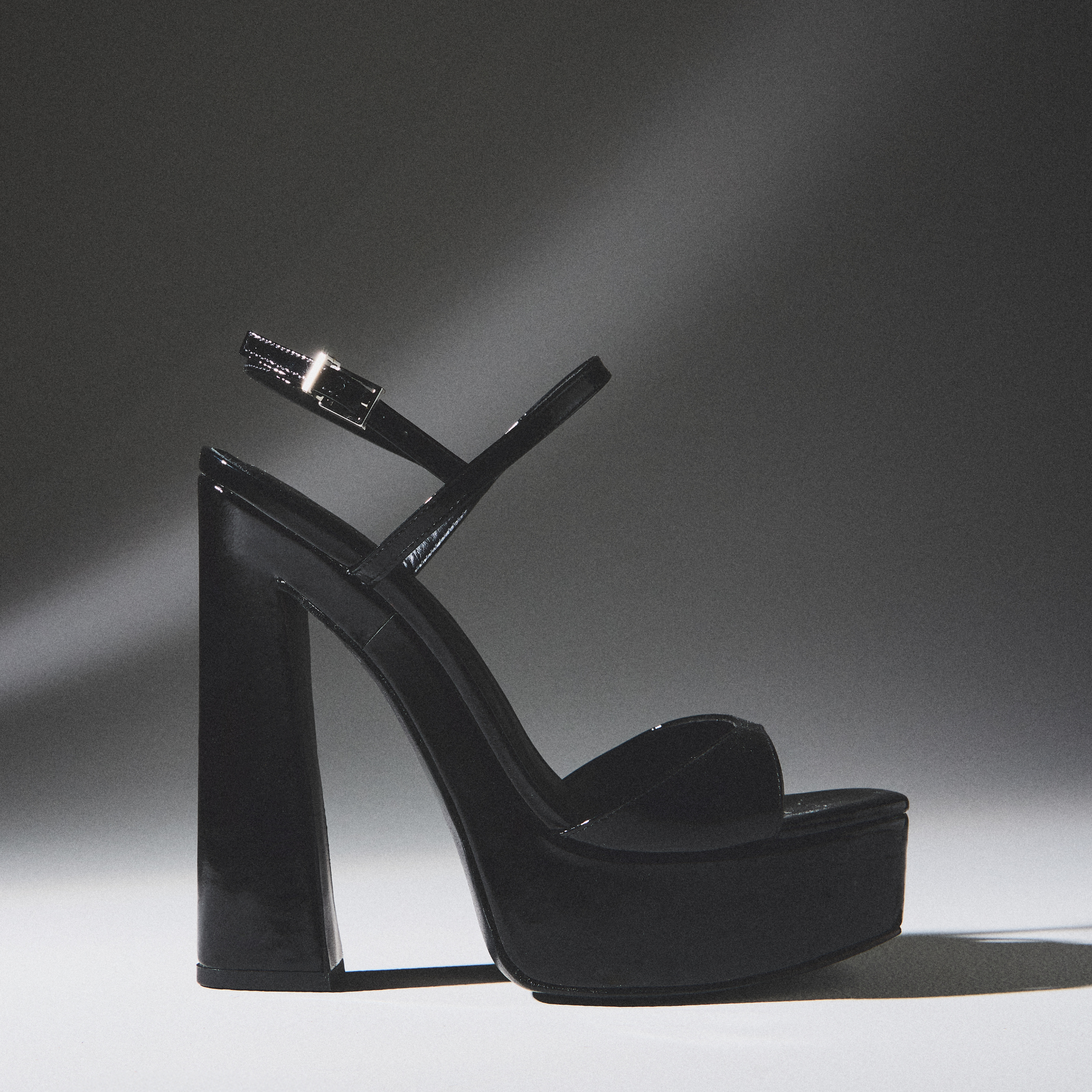 HIGH HEELS: Black patent leather platform sandal with a chunky block heel, thin ankle strap, and single toe strap, set against a dark, moody background. A "SHOP NOW" link is visible.