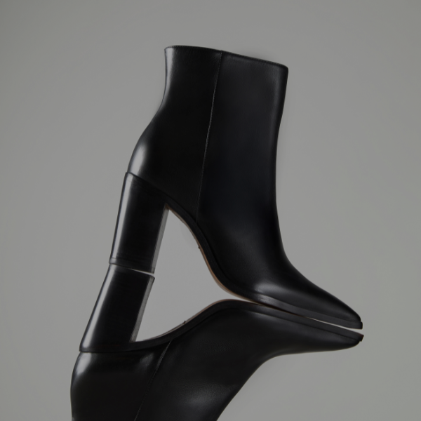 Pair of suede slouchy booties in a warm tan shade, displayed upright on the smooth edge of a bathtub. The boots have a pointed toe and a slim heel, styled in soft natural lighting.