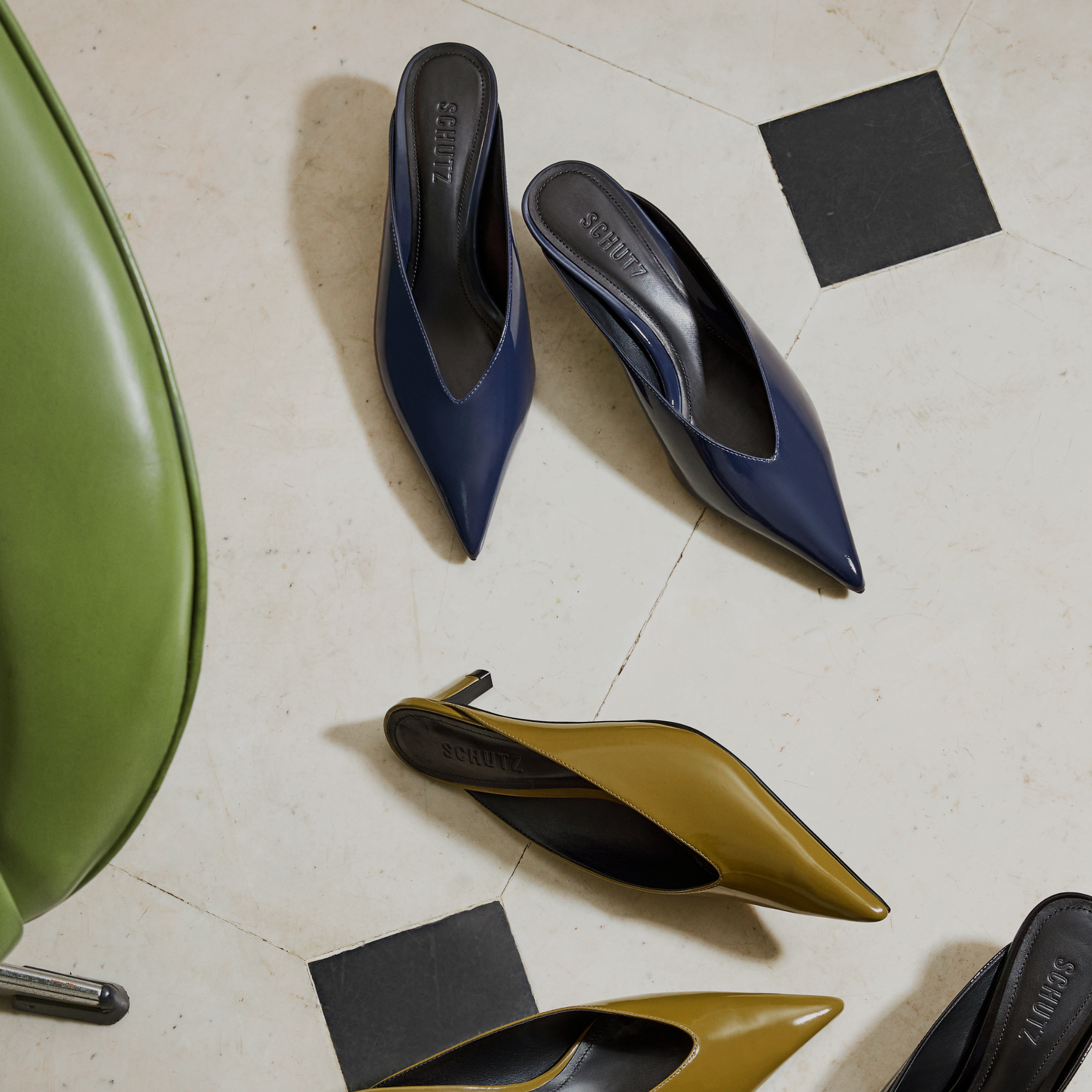 Advertisement for vacation wear featuring several pairs of navy, olive green, and black pointed-toe leather mule flats arranged on a tiled floor. Text overlay: "VACATION MODE" and "SHOP NOW" button.