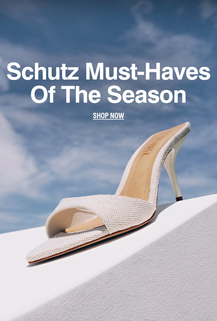 A stylish off-white textured high-heeled mule from Schutz, photographed against a blue sky and minimalist white architecture.