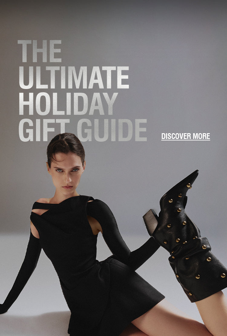 Woman wearing a stylish black dress and studded black boots posing on the floor against a gray background, next to the text “The Ultimate Holiday Gift Guide”.
