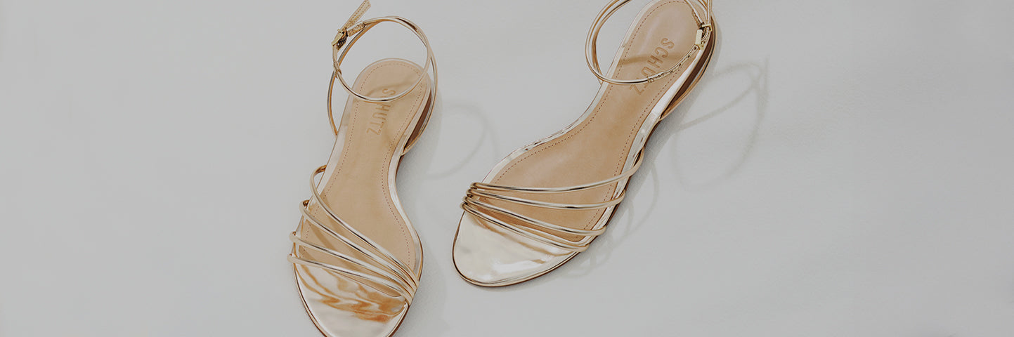 Pair of gold strappy flat sandals arranged on a light minimal background, highlighting elegant and versatile women’s flat sandal styles.
