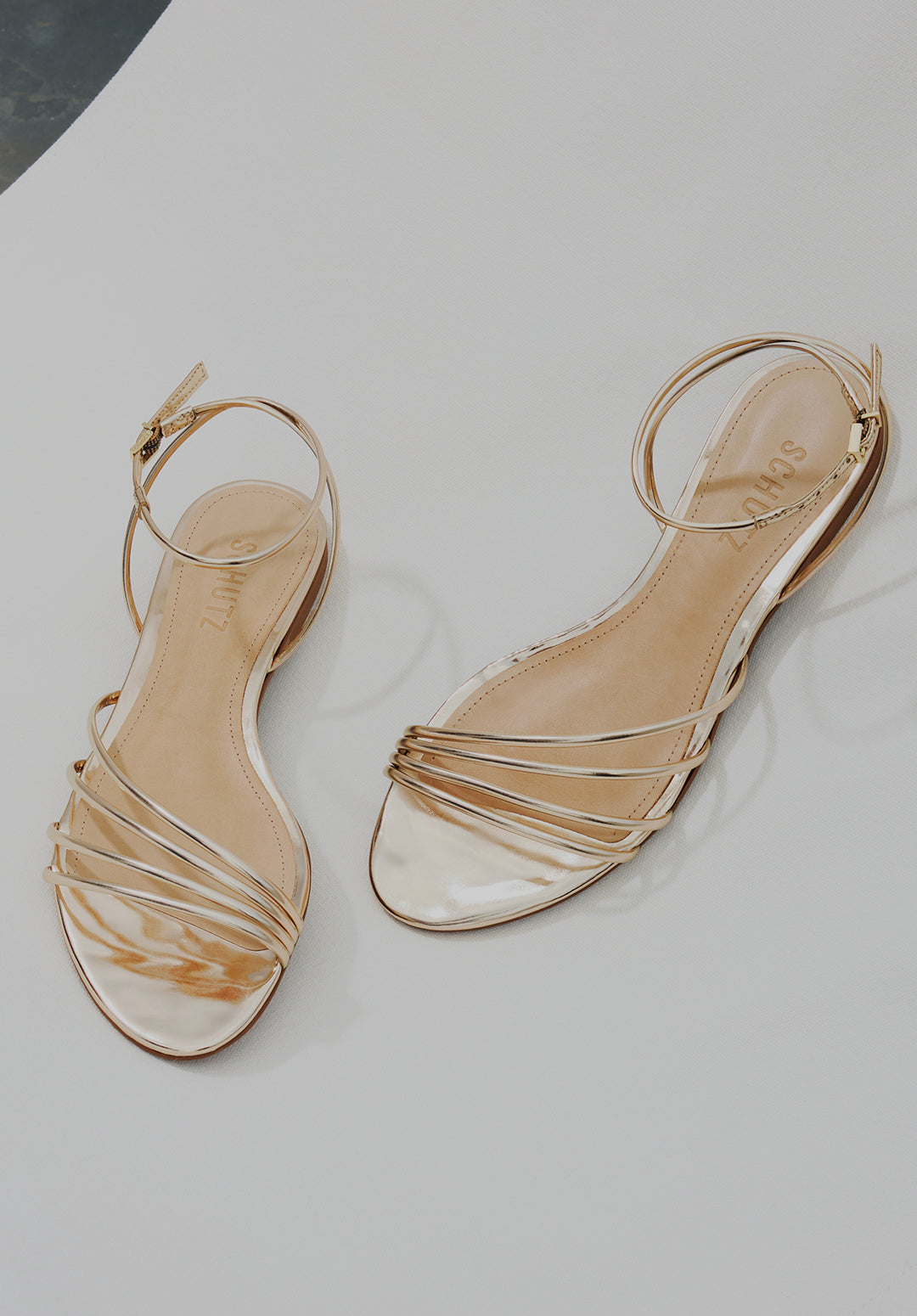 Pair of gold strappy flat sandals arranged on a light minimal background, highlighting elegant and versatile women’s flat sandal styles.
